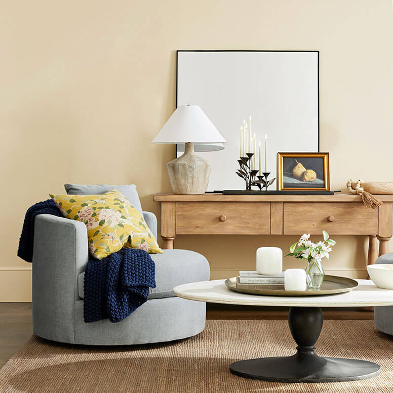 Pottery Barn living room with walls painted in Glad Yellow SW 6694, gray chair, large round coffee table, wooden table with lamp and other decor.