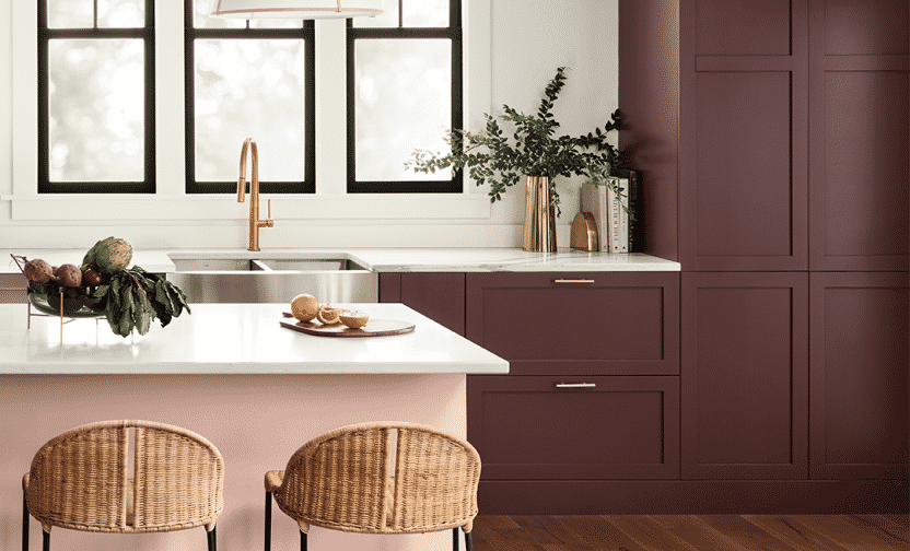 A kitchen with rich burgundy cabinets behind a light pink island with white countertop.