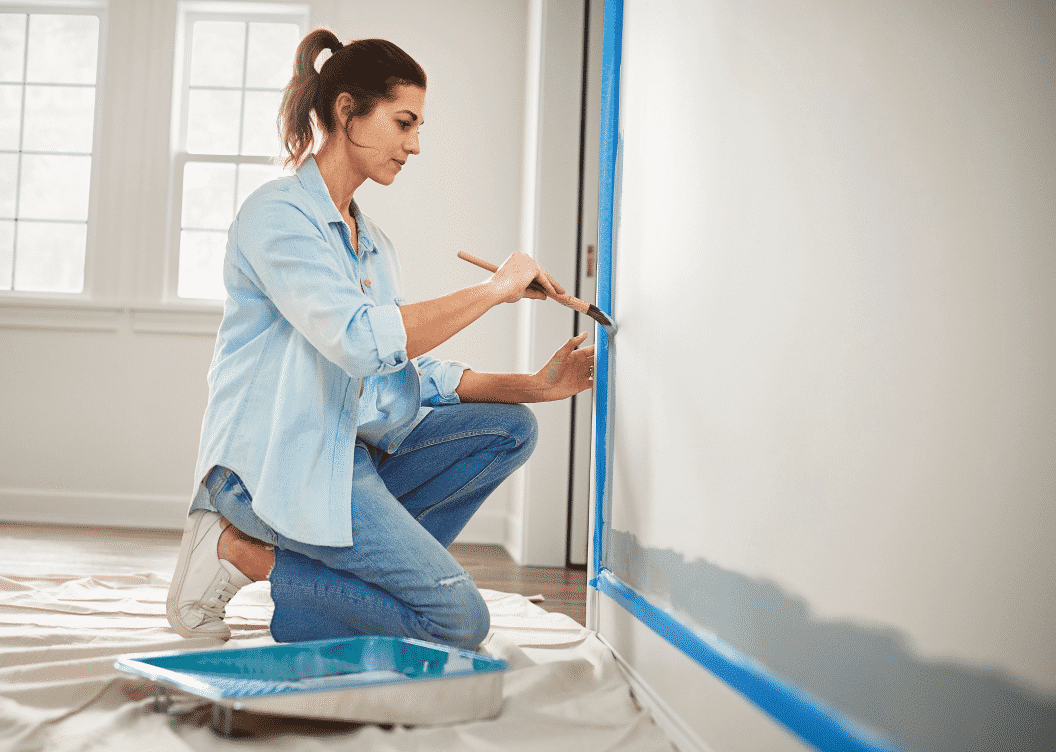 A person painting alongside trim that has blue painters tape applied.